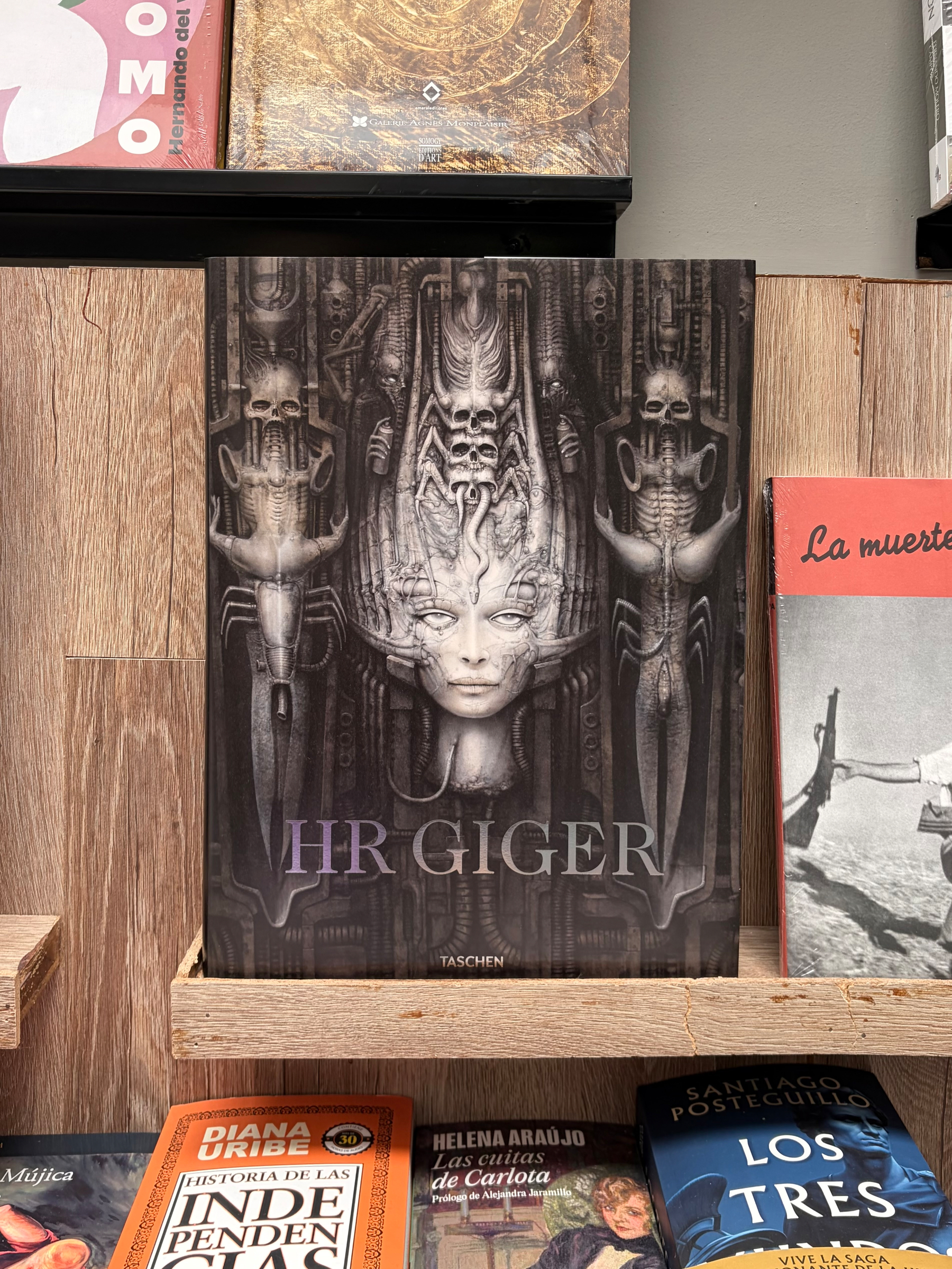 A biography and art book about HR Giger featuring his work displayed on a wooden shelf. On the cover: dark, surreal, biomechanical with a central humanoid face and skeletal figures.